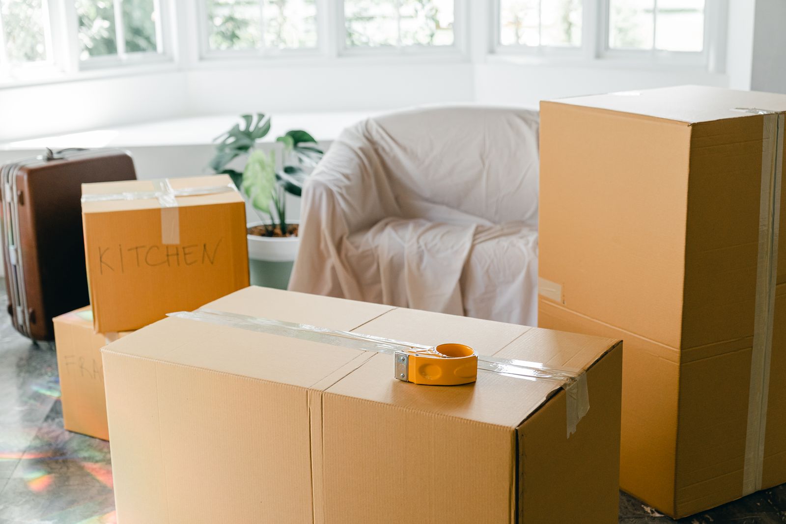 Packed boxes and a sheet-covered armchair in a sunlit room
