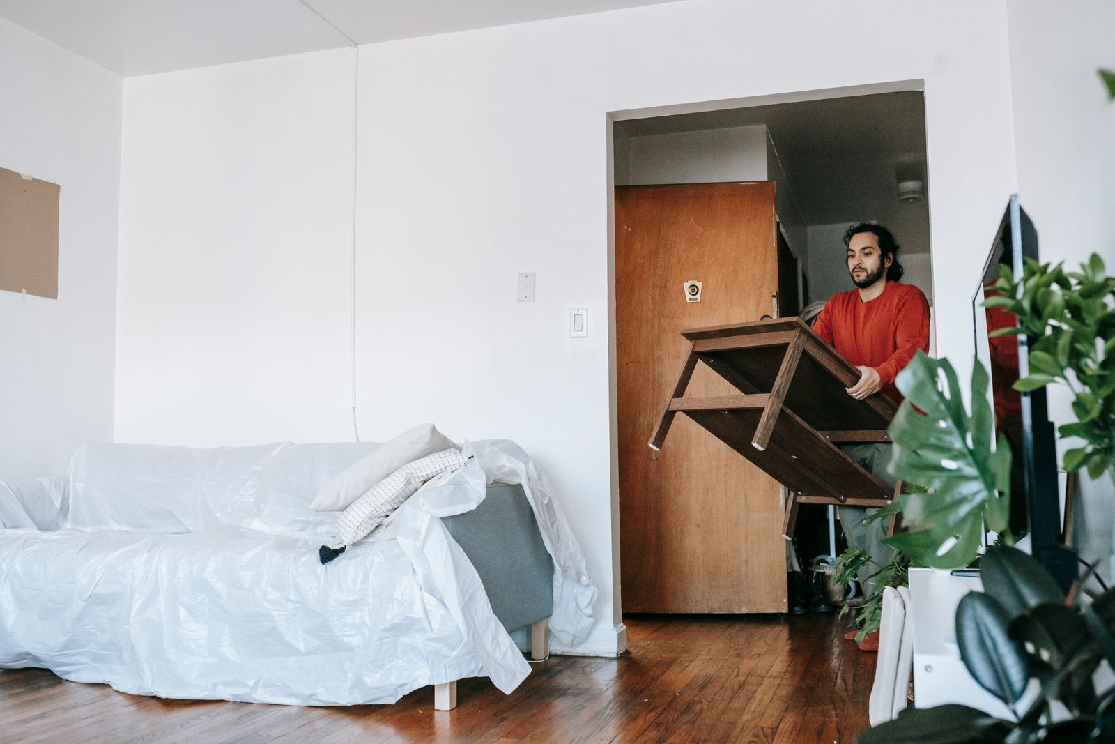 A man carrying a wooden table through a bright room during a move